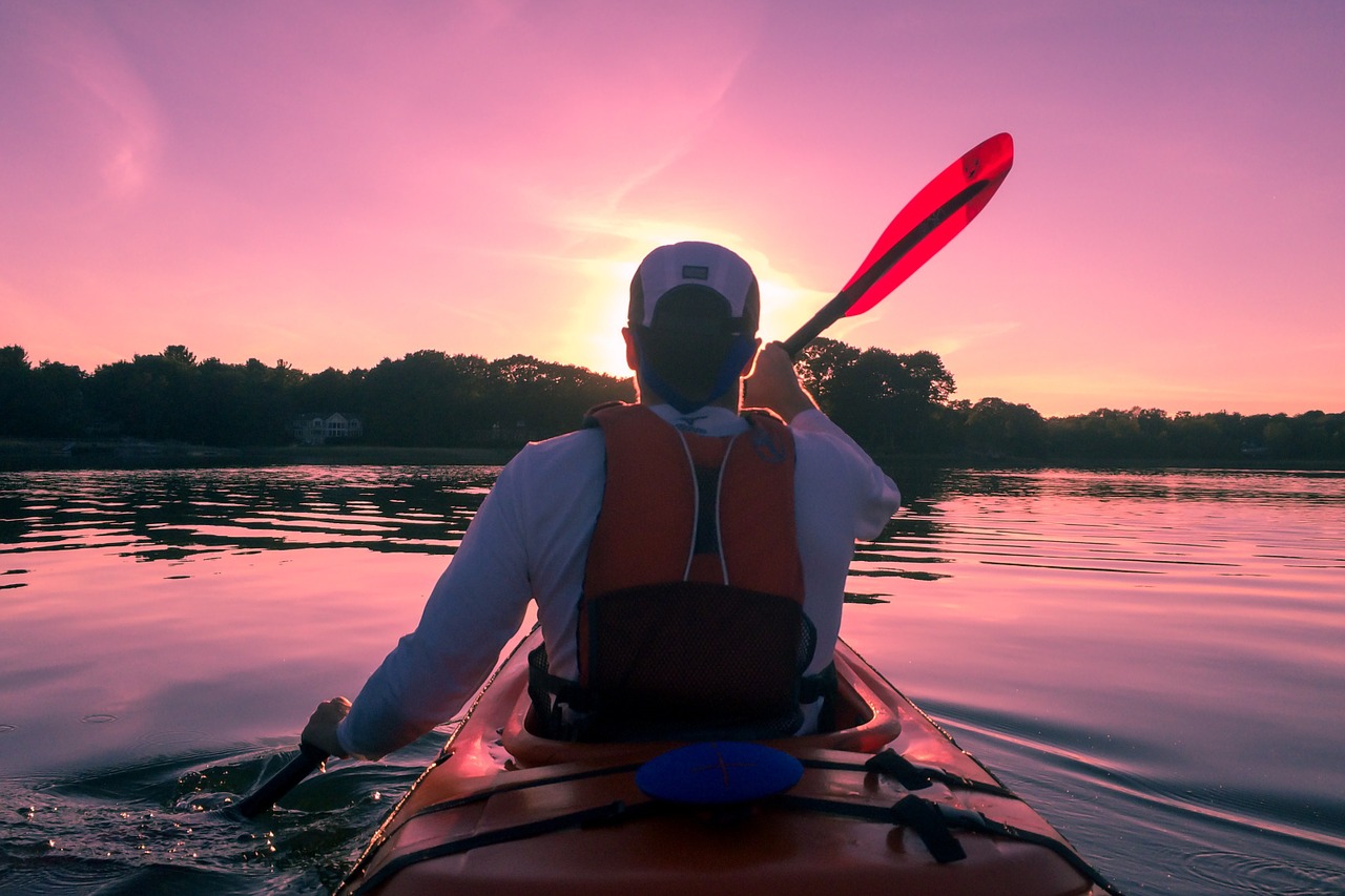 a man wearing a life vest calmly rowing on a lake staring into the sunset in Worcester Massachusetts